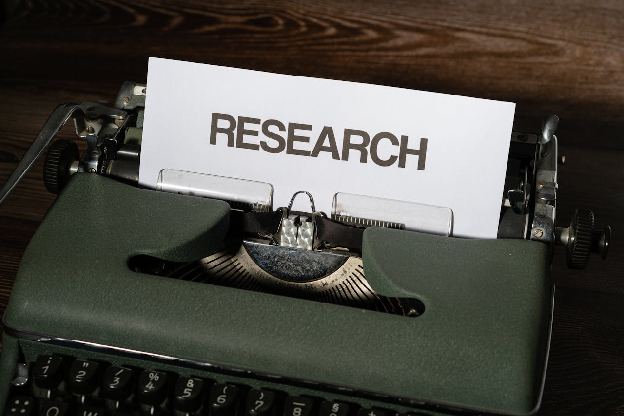 Close-up of a vintage typewriter with a paper labeled Research inserted, on a wooden surface.