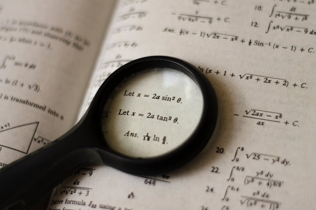 hero-img A magnifying glass focusing on mathematical equations in a textbook, symbolizing detailed study.